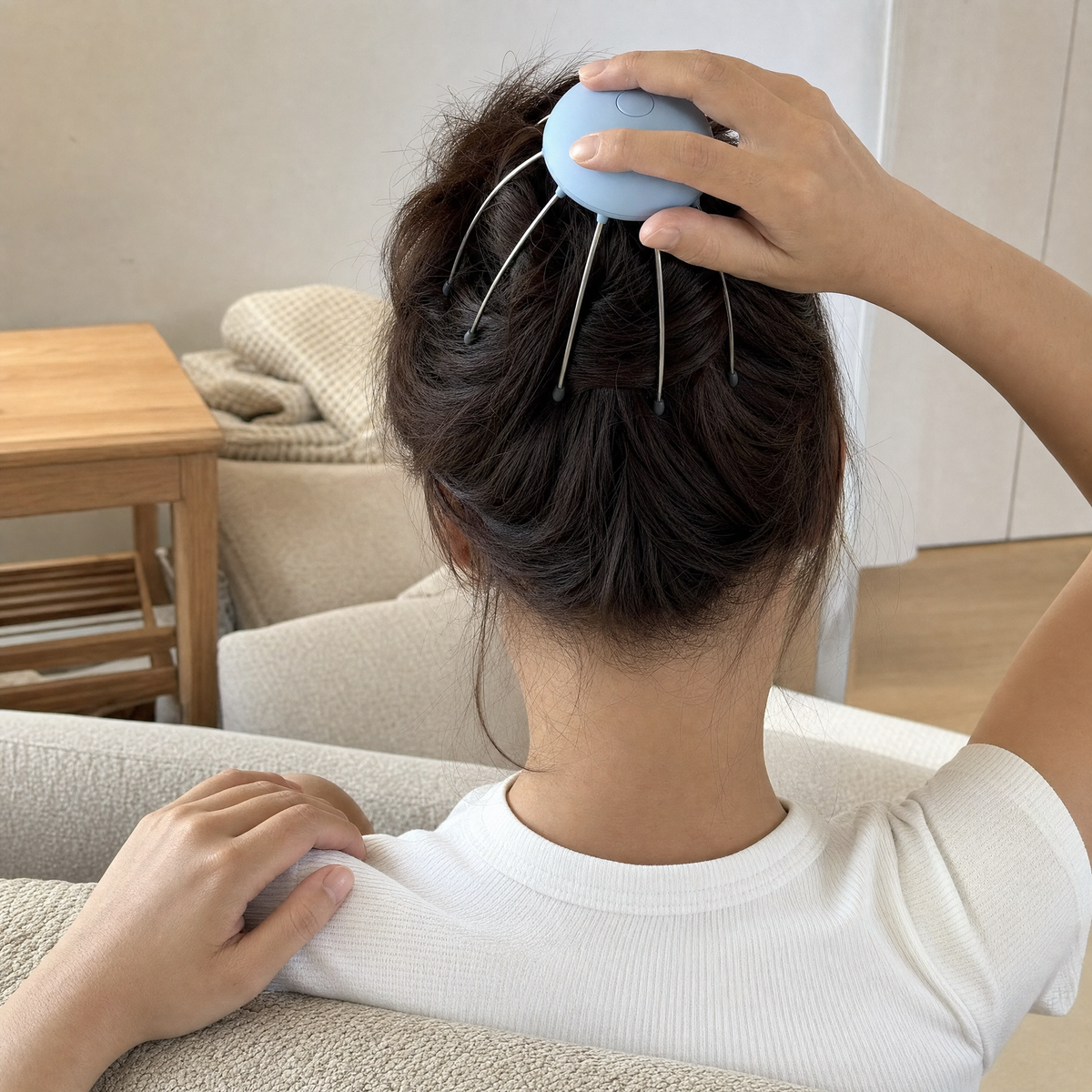 Woman using the 8-claw electric scalp massager on the crown of her head while sitting on a sofa