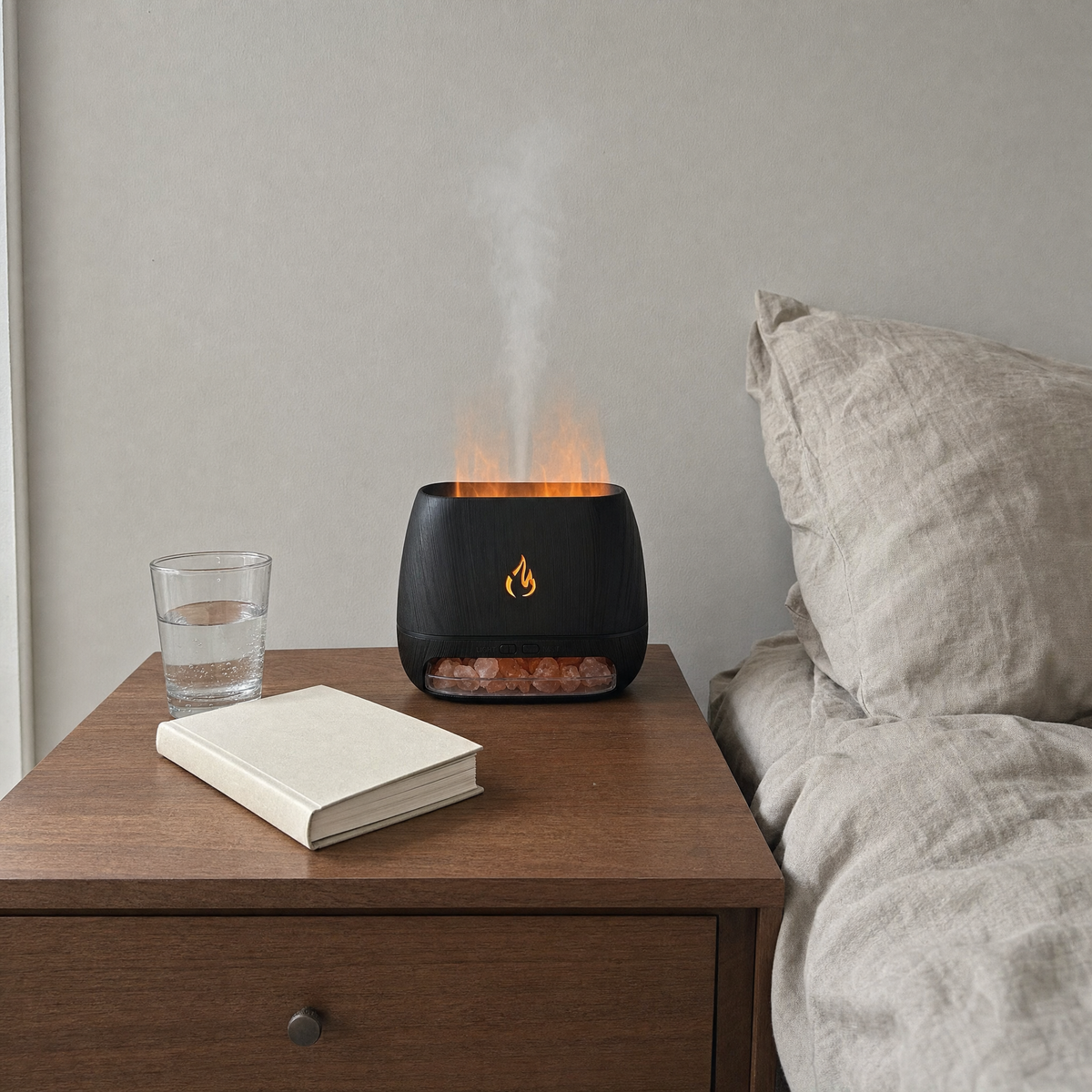 Flame effect aroma diffuser lit on a bedroom nightstand with mist rising, beside a book and a glass of water