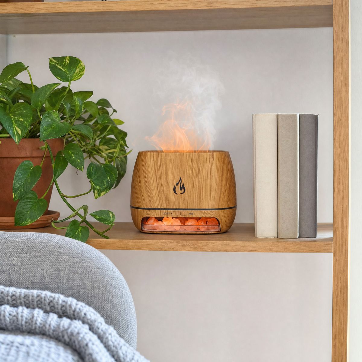 Flame effect essential oil diffuser on a living room bookshelf beside a trailing plant, flame glow and mist visible